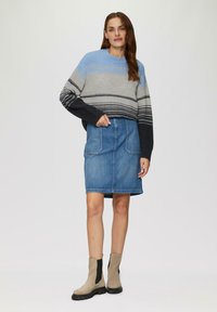 Häkelpullover in Grau und Blau, kombiniert mit einem Jeansrock und beigen Stiefeletten mit schwarzen Akzenten. Lässige Passform und strukturierter Strick.