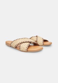 Woven fabric sandals in beige with dark stitch accents, featuring a flat sole and crossed straps for easy slip-on wear.