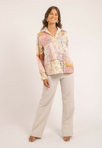 Blouse en soie multicolore avec des motifs floraux et paisley, avec col et boutonnière, associée à un pantalon large beige clair.