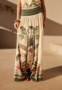 Falda larga y fluida en color crema con estampado tropical de hojas y animales en verde, rojo y rosa. Presenta una cintura fruncida y un dobladillo con patrón.