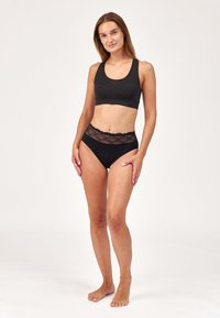 Soutien-gorge de sport en coton noir avec un col rond, associé à un slip noir taille haute avec une bordure en dentelle au niveau de la taille.