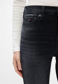 Sötétszürke, slim fit farmernadrág, öt zsebbel, gombos záródással és egy kis logóval a hátsó zsebben.