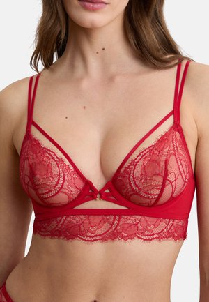 Roter Spitzen-BH mit floralen Mustern und doppelten dünnen Schulterriemen, getragen von einer Frau, die Oberkörper und Dekolleté zeigt.