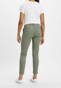 Olivgrön, slim-fit byxor med medelhög midja och bakfickor, ihopparade med en vit t-shirt med kort ärm och vita sneakers.