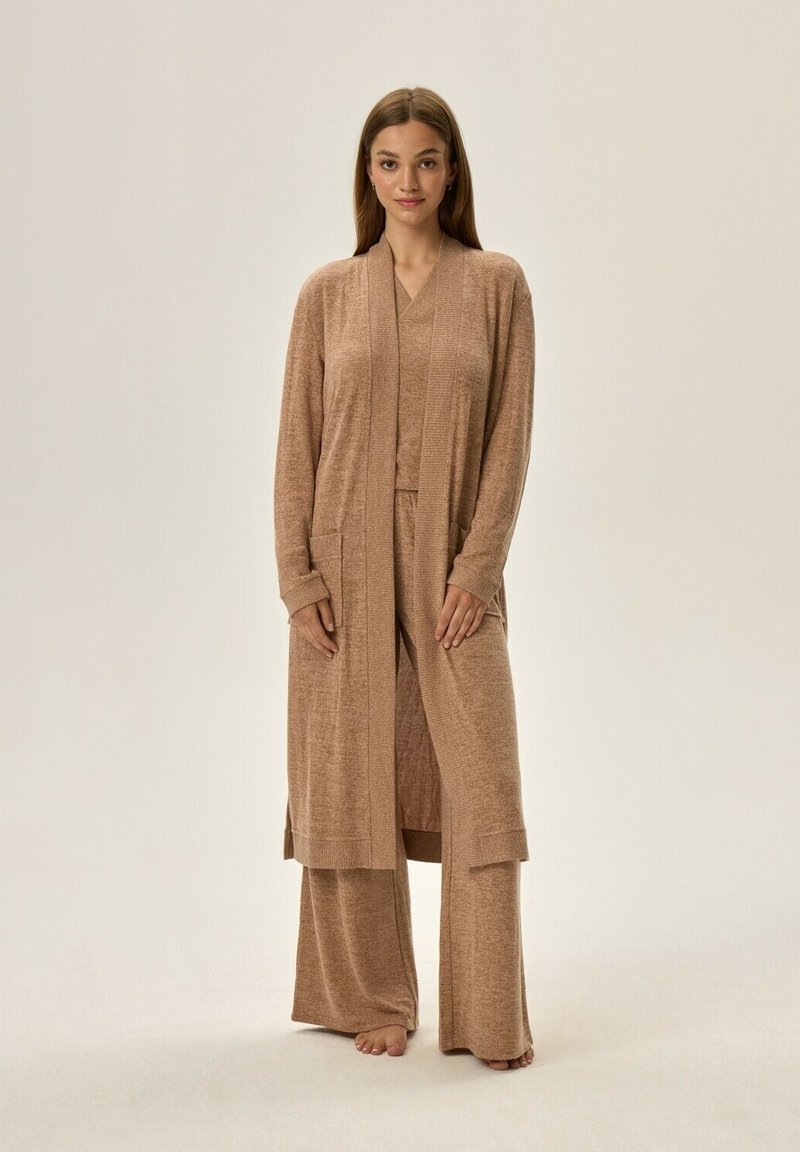 Jasnobrązowy zestaw odzieży domowej składający się z długiego kardiganu z kieszeniami, bluzki z dekoltem w serek oraz luźnych spodni wykonanych z miękkiego, teksturowanego materiału.