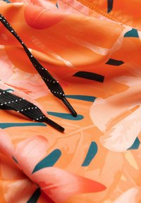 Gros plan de lacets noirs à pois blancs sur un tissu orange orné de motifs floraux abstraits roses et bleu sarcelle.