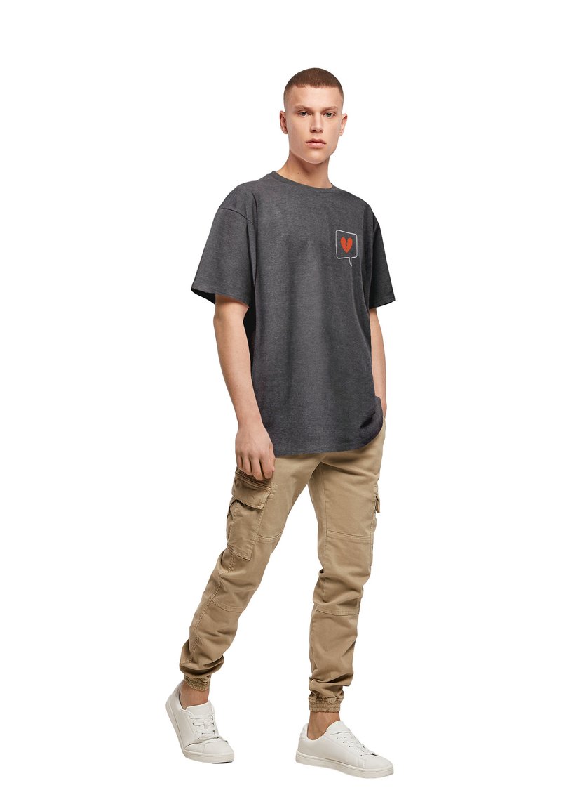 Grå bomulds t-shirt med et logo på venstre bryst, parret med beige cargo bukser med sidelommer og elastiske manchetter, afsluttet med hvide sneakers.