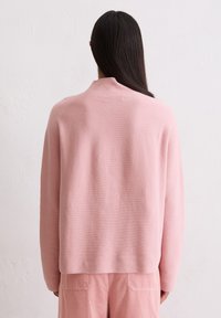 Lichtroze, oversized trui met een ontspannen pasvorm, textuurgebreide stof en een hoge hals, gedragen met bijpassende lichtroze corduroy broek.