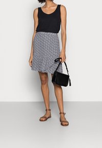 Svart linne, blommönstrad kjol i blått och vitt, bruna sandaler och en liten svart handväska med en tofs.