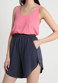 Różowy top na ramiączkach o szerokich paskach, zestawiony z ciemnoniebieskimi szortami z elastycznym pasem i bocznymi kieszeniami, wykonany z miękkiego materiału i o luźnym kroju.