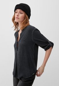 Czarna, soft shirt z dekoltem w kształcie litery V, z podwiniętymi rękawami zabezpieczonymi guzikami i zaokrąglonym dołem. Noszona z ciemnymi dżinsami i czarną czapką beanie.