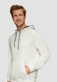 Sweatshirt à capuche blanche avec une poche avant, des cordons noirs et blancs, et une doublure intérieure grise. Présente un minimalisme dans le branding sur la poitrine.
