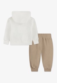 Witte katoenen hoodie en beige joggingbroek. Voorzien van geribbelde manchetten en tailleband, zachte textuur en een comfortabele pasvorm.