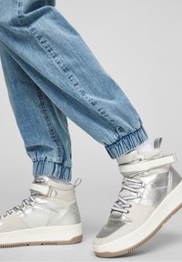 Zapatillas altas plateadas con un acabado texturizado, cordones blancos y acentos en gris claro contrastantes; combinadas con unos pantalones jogger azul ajustados.