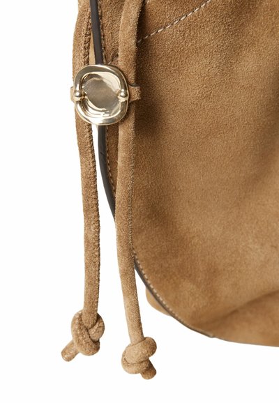 Detalle de una bolsa de ante marrón con un cierre de metal dorado, material texturizado, cierre de cordón y nudos decorativos en las correas.