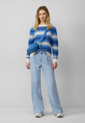 Niebieski sweter w paski, szerokie jasnoniebieskie dżinsy i mała niebieska torebka na ramię. Całość dopełniają białe sneakersy.