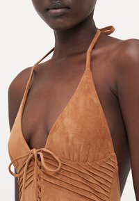 Brown suede halter neck dress with triangular cups, gathered texture, and a lace-up front. Features thin straps and a smooth finish.