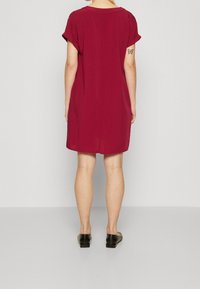 Robe courte bordeaux, manches courtes, coupe ample, tissu léger. Paire de chaussures noires, design simple. Pas de motifs ni ornements visibles.