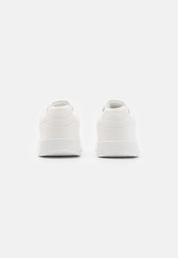 Weiße Sneakers mit einer glatten synthetischen Oberfläche, abgerundeten Fersen und strukturierten Gummisohlen. Minimalistisches Design, ohne sichtbare Markenkennzeichnung.