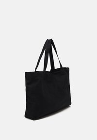 Svart canvas tote-väska med två handtag på toppen, rektangulär form och mjuk textur med en minimalistisk design.