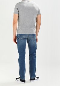 Šedé tričko s krátkým rukávem, modré džínové džíny, černé tenisky s bílými pruhy. Na džínách jsou viditelné švy, volný střih.