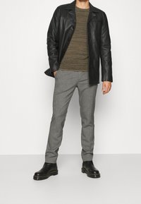 Schwarze Lederjacke, olivgrün gestreiftes Langarmhemd, graue maßgeschneiderte Hose und schwarze ankle Boots mit dicker Sohle.