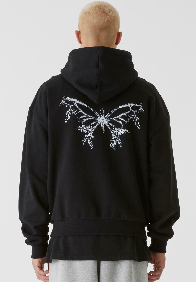 Svart hoodie med en stor vit fjärilsbild på ryggen, långa ärmar, en justerbar huva och en lager-på-lager nederkant.