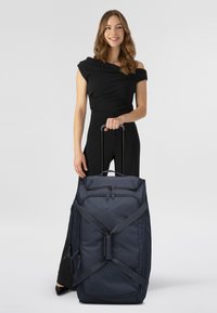 Sac de sport à roulettes bleu marine, fabriqué en tissu durable, doté de double zip, de poignées réglables et d'une poignée supérieure pour un transport facile.