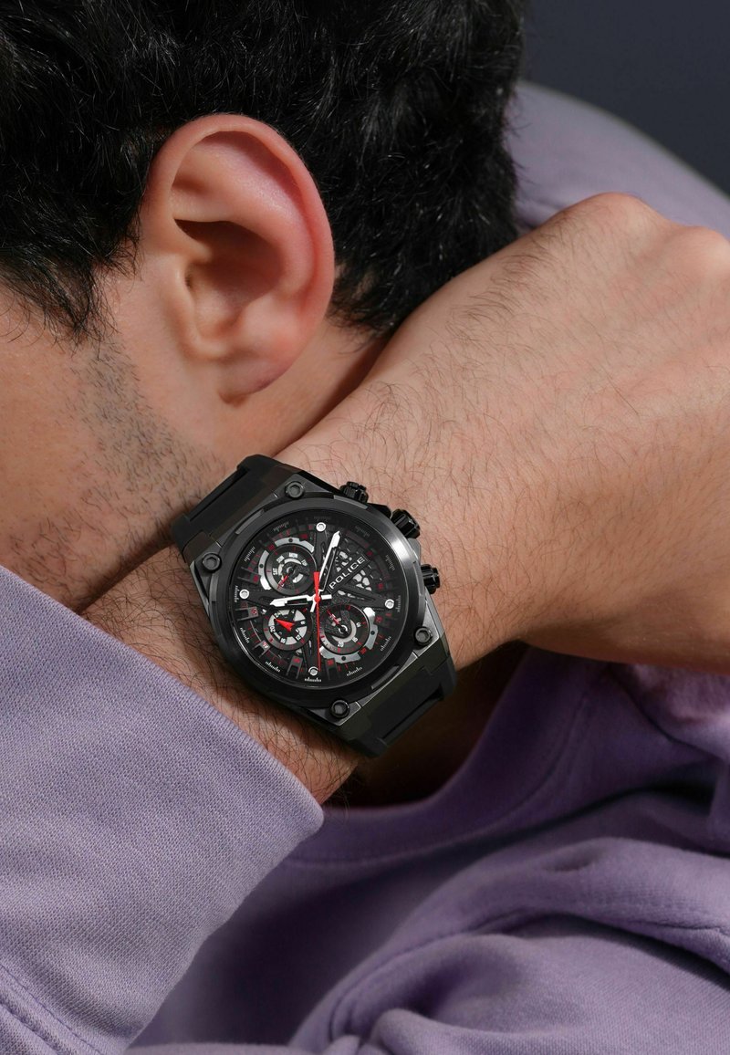 Orologio sportivo nero con una lunetta testurizzata, quadrante scuro a più strati, dettagli rossi e cinturino in gomma, indossato su un polso.