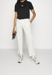 Svart croppad t-shirt med en liten vit logotyp, kombinerad med off-white avslappnade byxor och ljusa sneakers.