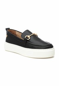 Zapatos negros de cuero tipo slip-on con una suela de plataforma blanca, que cuentan con un acento de cadena dorada en la parte frontal y un forro interior texturado.