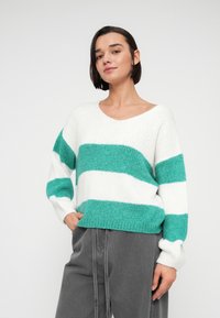 Pull en maille à rayures blanches et bleu sarcelle avec un col en V, des manches longues et une coupe décontractée. Texture douce et détail de bord-côte à l'ourlet.