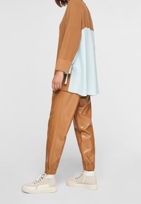 Hnědý a světle modrý oversized top s žebrovanou texturou, spárovaný s tanovým umělým koženým kalhotami a béžovými vysokými teniskami.