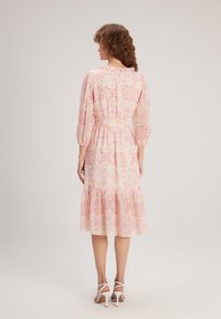 Robe longue en tissu floral rose avec des manches bouffantes, une taille élastique et un ourlet à volants en tiers. Présente un motif floral délicat dans des teintes claires.