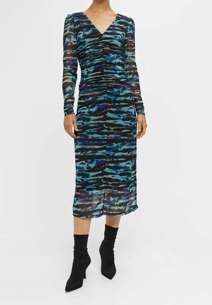 Femme portant une robe midi froncée à manches longues avec des motifs abstraits bleus et noirs, associée à des bottines noires à bouts pointus.
