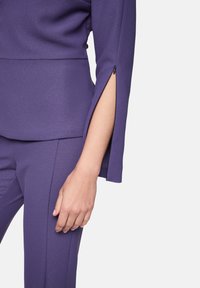 Purple two-piece suit featuring a fitted top with a split sleeve design and smooth texture, paired with tailored pants.