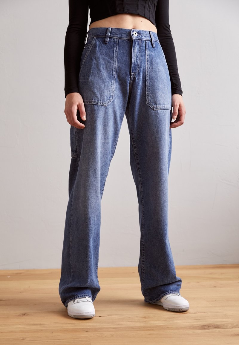 Ljusblå denim cargo-byxor med en avslappnad passform, som har stora framfickor och knäppning, kombinerat med vita sneakers.