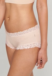 Ropa interior hipster de color rosa claro, fabricada con una tela suave, que presenta un delicado encaje en la cintura y en las aberturas de las piernas. Textura suave en general.