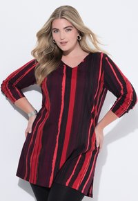 V-neck tunic in a burgundy fabric with vertical red and black stripes, featuring three-quarter sleeves and side slits for ease of movement.