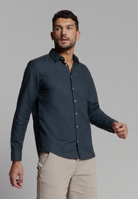 Donker marineblauwe blouse met lange mouwen en button-down kraag, met een subtiele textuur en contrasterende knopen, gecombineerd met lichtbeige broek.