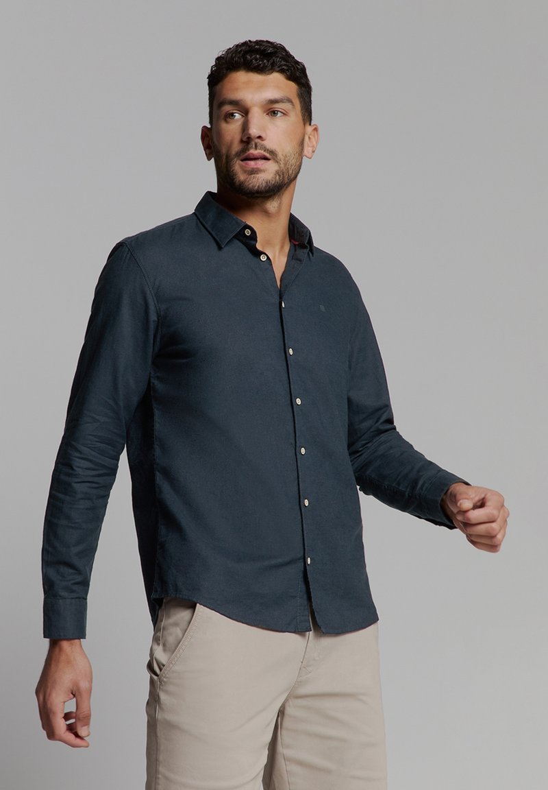 Donker marineblauwe blouse met lange mouwen en button-down kraag, met een subtiele textuur en contrasterende knopen, gecombineerd met lichtbeige broek.