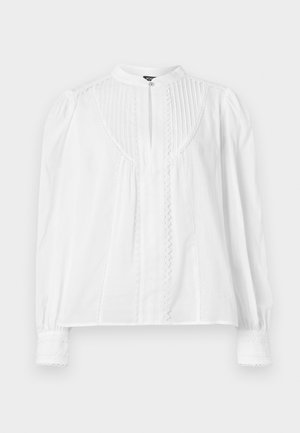 Blouse blanche à manches longues avec col mandarin, plis verticaux, détails en dentelle sur le devant et les poignets, et une fermeture par un bouton unique au niveau du cou.