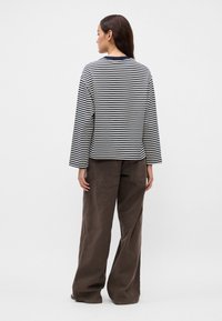 Ριγέ μακρυμάνικο μπλουζάκι σε μαύρο και άσπρο, με στρογγυλή λαιμόκοψη, άνετη εφαρμογή και ορατές ραφές, συνδυασμένο με καφέ παντελόνια φαρδιάς γραμμής.
