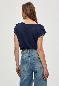 Camiseta de manga corta azul marino con un corte relajado; combinada con jeans de cintura alta azul claro que cuentan con dos bolsillos traseros y costuras visibles.