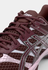 Bordo tekaški čevelj z mrežasto zgornjim delom, teksturiranim dizajnom in srebrnimi detajli. Ponaša se z izrazitimi vezalkami in oblazinjenim podplatom.