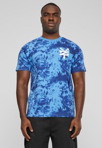 Blå tie-dye T-skjorte laget av bomull, med rund hals og korte ermer. Utsatt hvit grafisk design på brystet.
