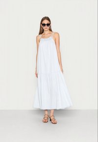 Vestido maxi azul claro com um design em camadas, alças finas e decote franzido. Acompanhado de sandálias com tiras e óculos de sol redondos.