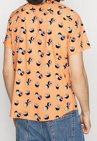 Short-sleeve shirt in orange fabric featuring a repeated sushi print in black, white, green, and red accents. Casual fit with a curved hem.