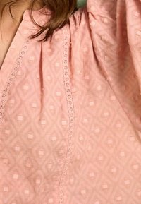 Blusa rosa con un motivo a diamante testurizzato e piccole square. Maniche a palloncino decorate con un delicato pizzo lungo lo scollo.