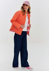 Pruhovaná oranžová prešívaná bunda, biela blúzka, tmavé denimmové nohavice širokého strihu, ružové športové topánky s tromi pruhmi, svetloružová čiapka.